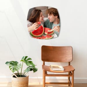 Suporte de espelho decorativo com imagem de casal com melancia, parede branca, cadeira de madeira e planta.